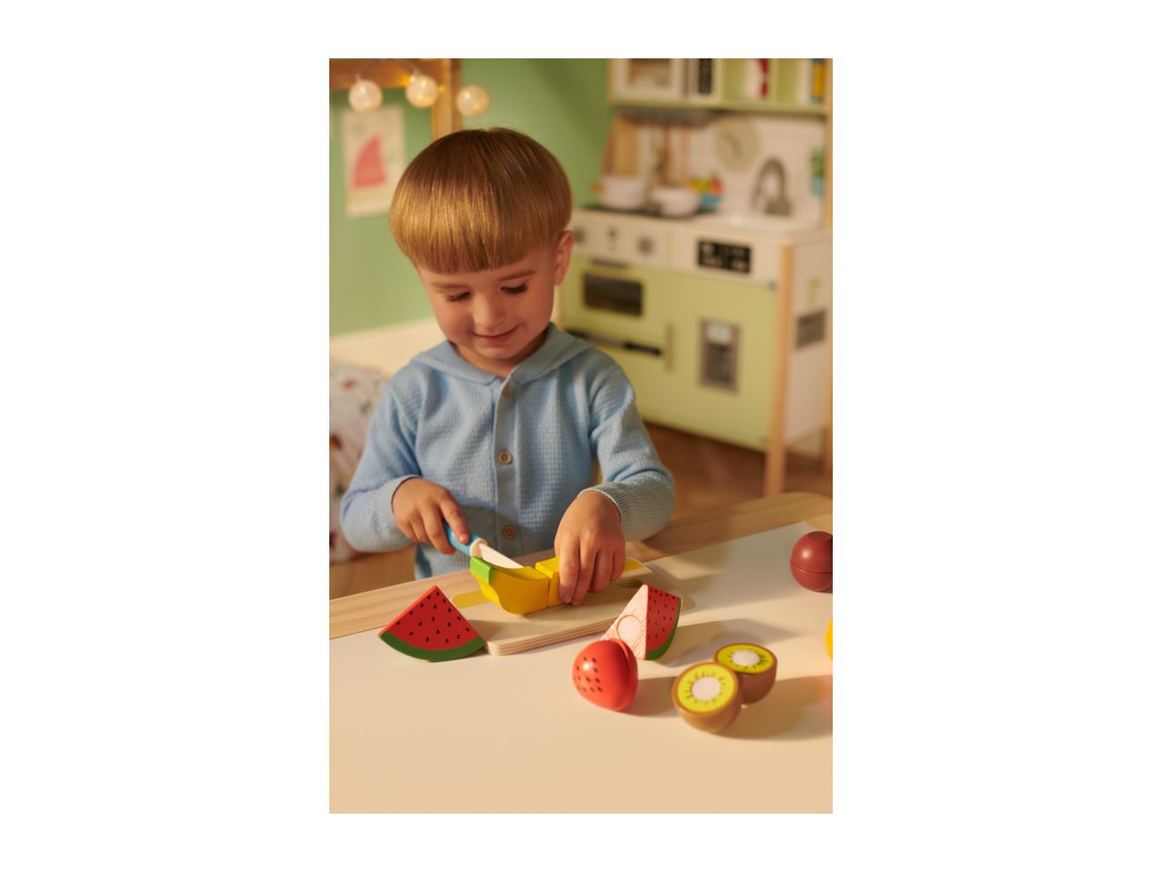 A child playing with wooden toy fruit, cutting a banana on a chopping board.