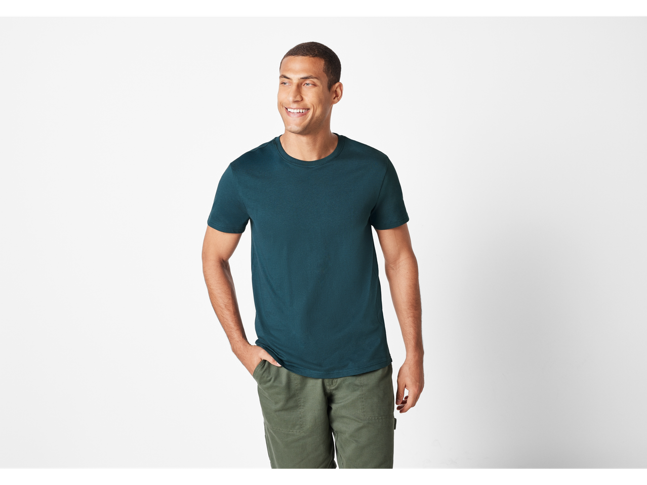 Homem sorridente vestindo uma camiseta verde-escura e calças verdes.