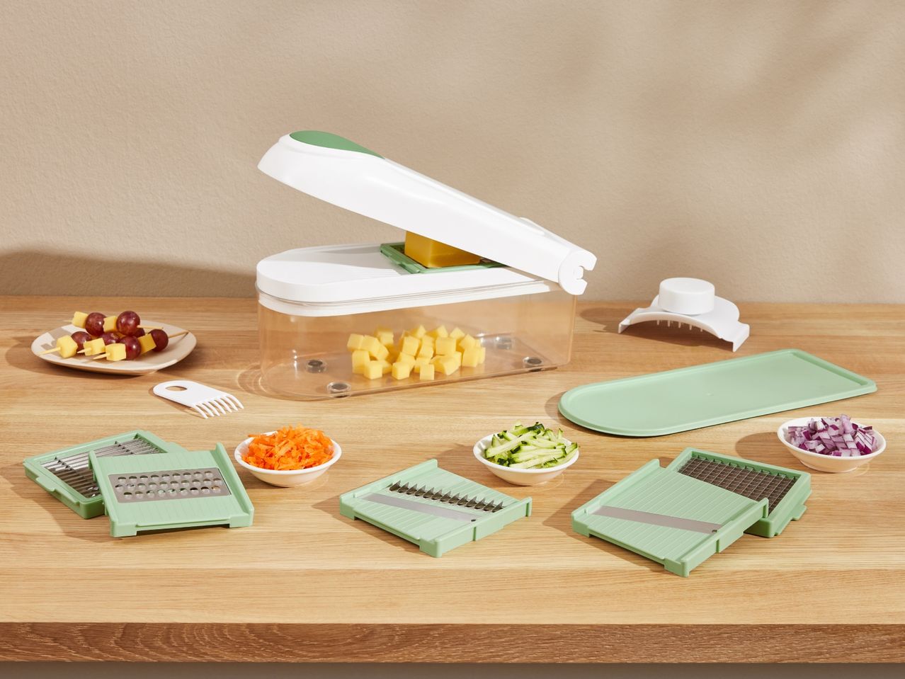 A vegetable chopper and various cutting attachments are displayed on a wooden surface.