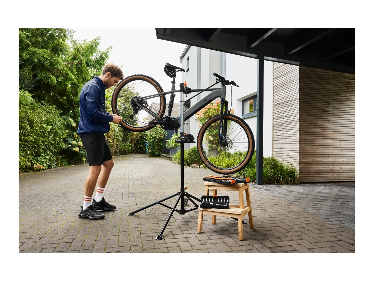 Man repairing a bicycle on a repair stand with tools on a stool outdoors.