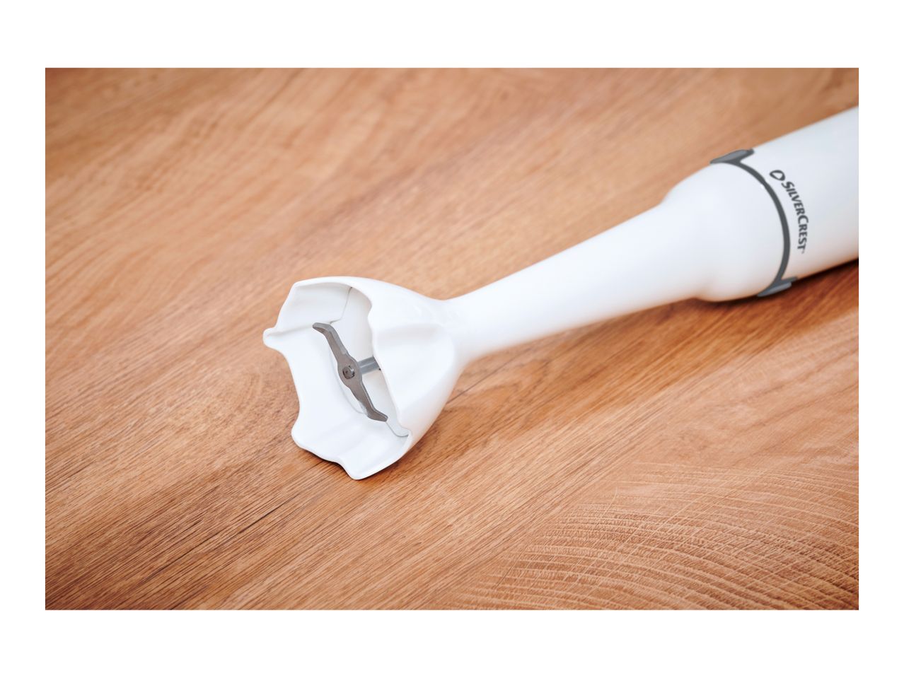White immersion blender with a metal blade on a wooden surface.