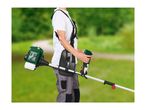 Person operating a petrol brush cutter with a harness in a garden setting.