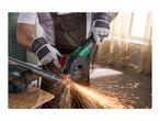 Person in work overalls and gloves cutting a metal pipe with an angle grinder, creating sparks.