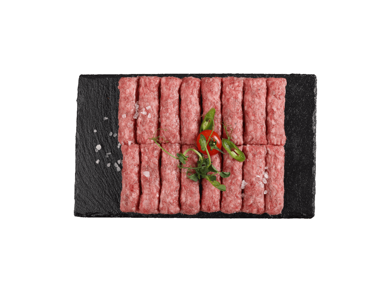 Sveži ćevapi na crnoj ploči sa solju, paradajzom i zelenim začinskim biljem.