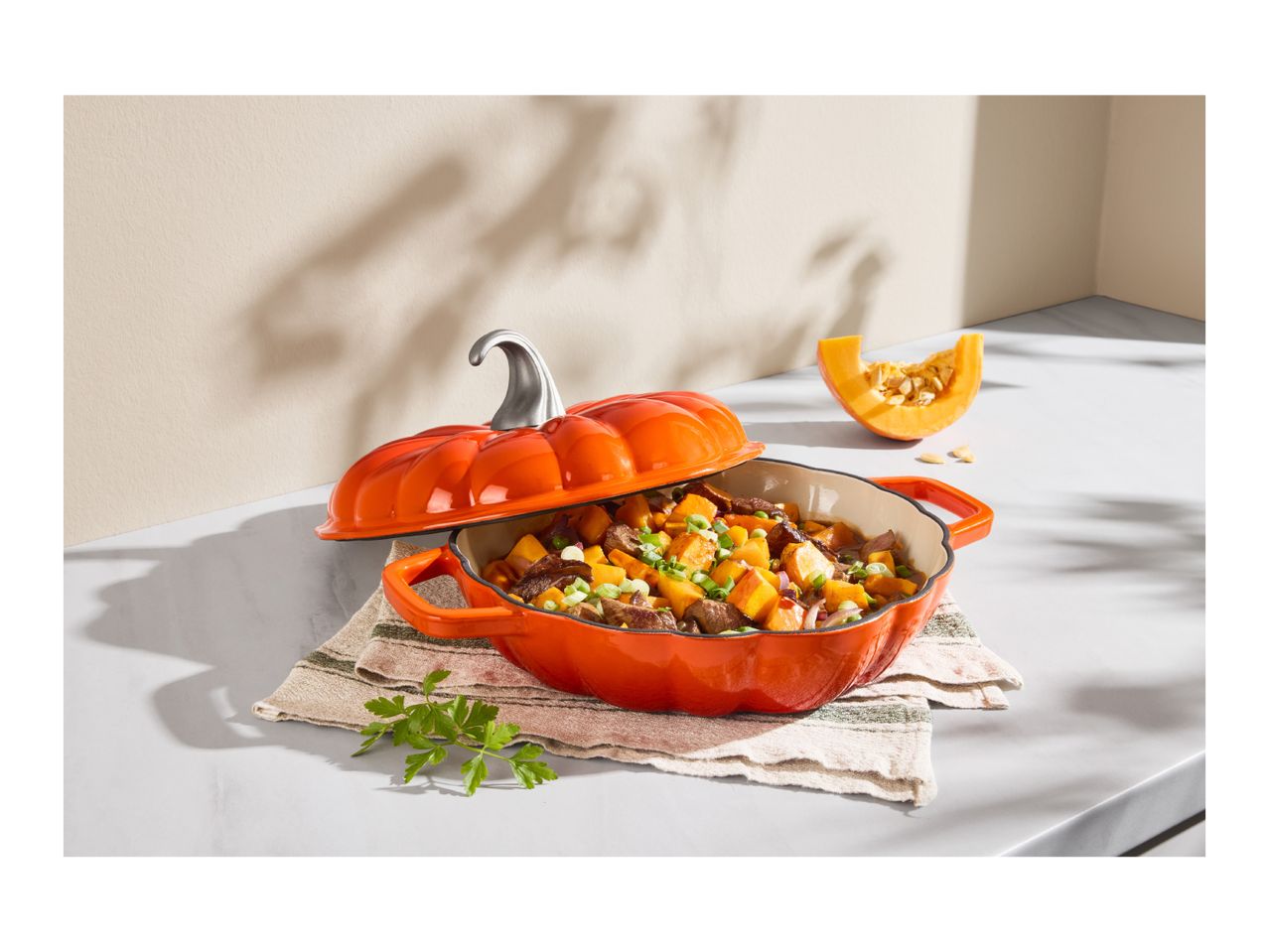 Pumpkin-shaped cast iron casserole dish filled with stew on a kitchen counter