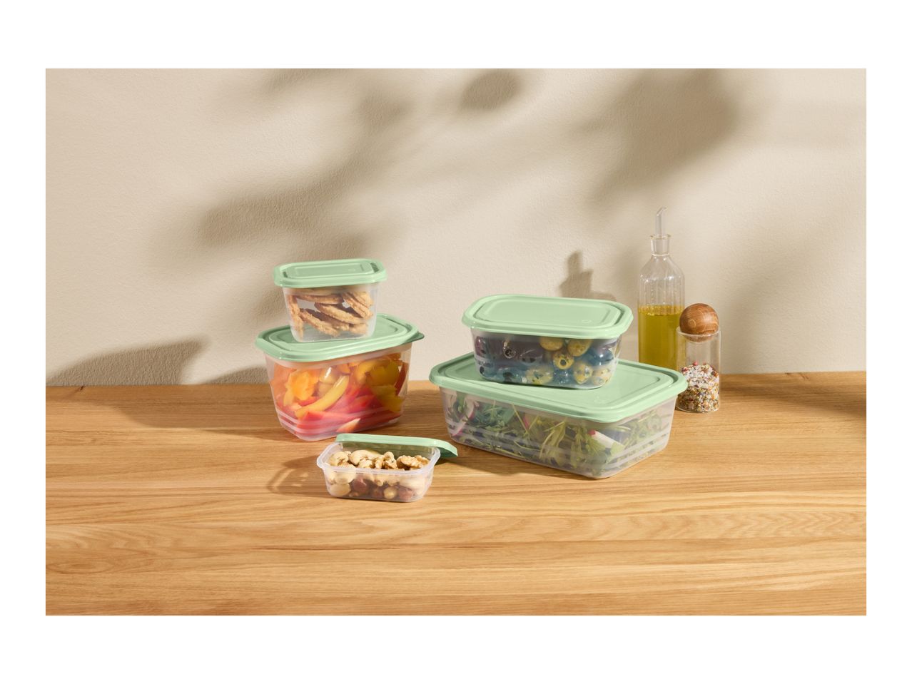 Food storage containers with green lids, filled with snacks, vegetables, and salad.