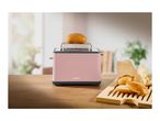 Pink SilverCrest toaster with a bun on top, and more buns on a wooden board.