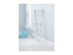 White foldable clothes drying rack leaning against a light blue wall, with a laundry basket.