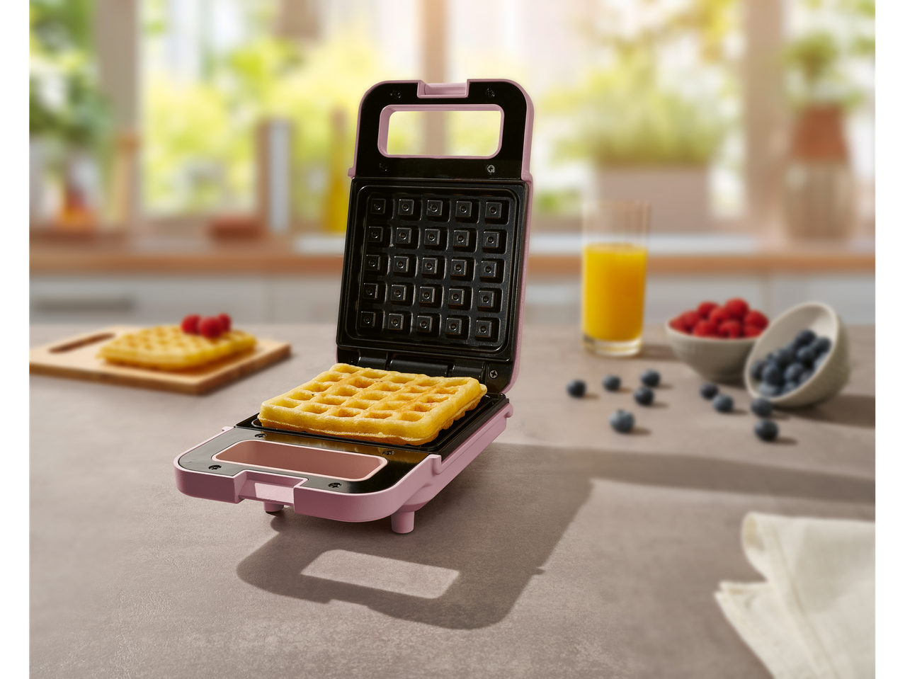 Rožinis mini vaflinis keptuvėlis su ką tik iškepta vafliu.