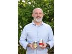 A man holding two cans of Steeper Culture kombucha, 'The Haymaker' and 'Cherry Lime' flavors.
