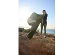 Woman holding a CRIVIT Mummy Sleeping Bag on a rocky coast with the sea in the background.