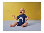 Happy baby in a blue shark-themed outfit, sitting on a light blue surface with bubbles.