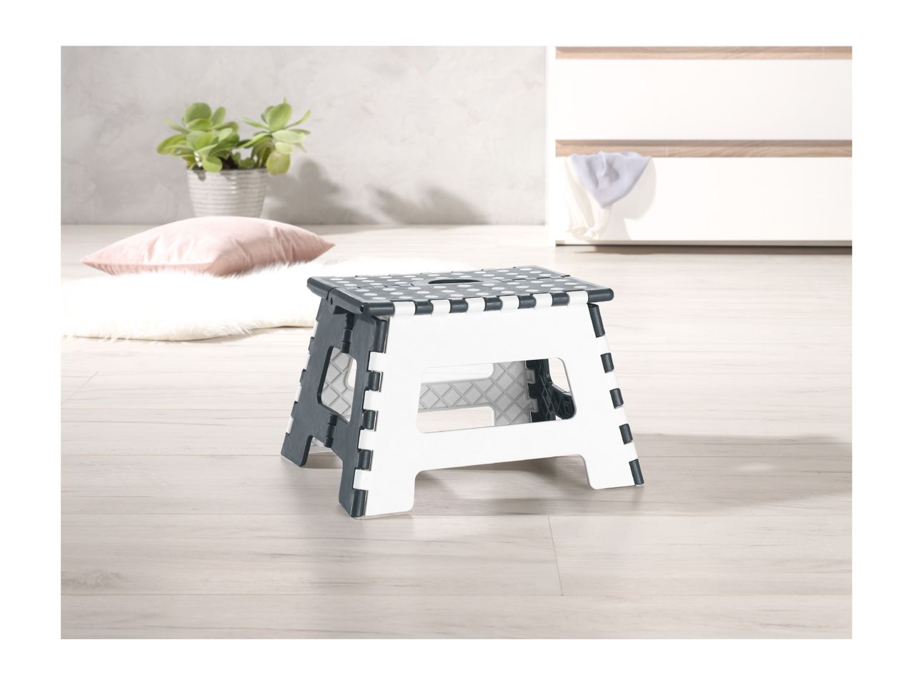 A foldable plastic step stool in white and dark gray sits on a light wood floor.