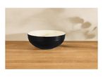 Black and white bowl on a wooden table with plant shadows on the wall.