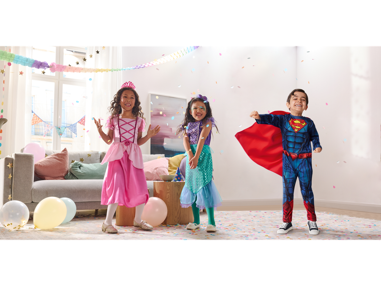 Drei Kinder in Prinzessinnen-, Meerjungfrauen- und Superman-Kostümen mit Konfetti.