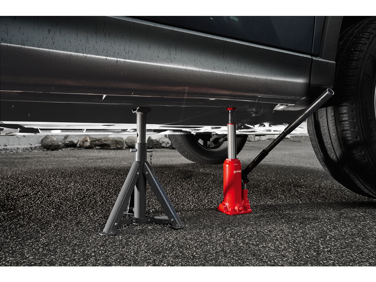 A car is lifted by a red hydraulic jack and supported by a grey jack stand.