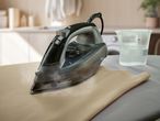A SilverCrest steam iron on an ironing board with a measuring cup of water.