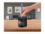 A hand inserts a blue pencil into a black electric pencil sharpener on a wooden table.
