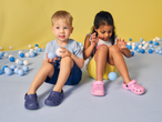 Two children in blue and pink clogs playing with blue and white balls.