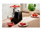 A black electric meat grinder processing tomatoes into a bowl of sauce on a wooden counter.