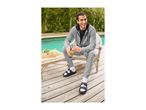 Man in grey tracksuit and black sandals with white socks, holding a green smoothie by a pool.