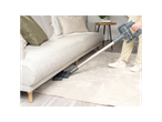 A person cleans under a sofa with a cordless vacuum cleaner.