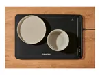 Black electric warming tray with a plate and bowl on a wooden table.