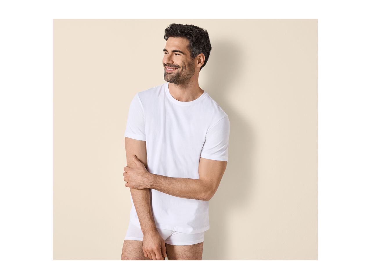Man in white t-shirt and underwear, smiling and looking to the side.