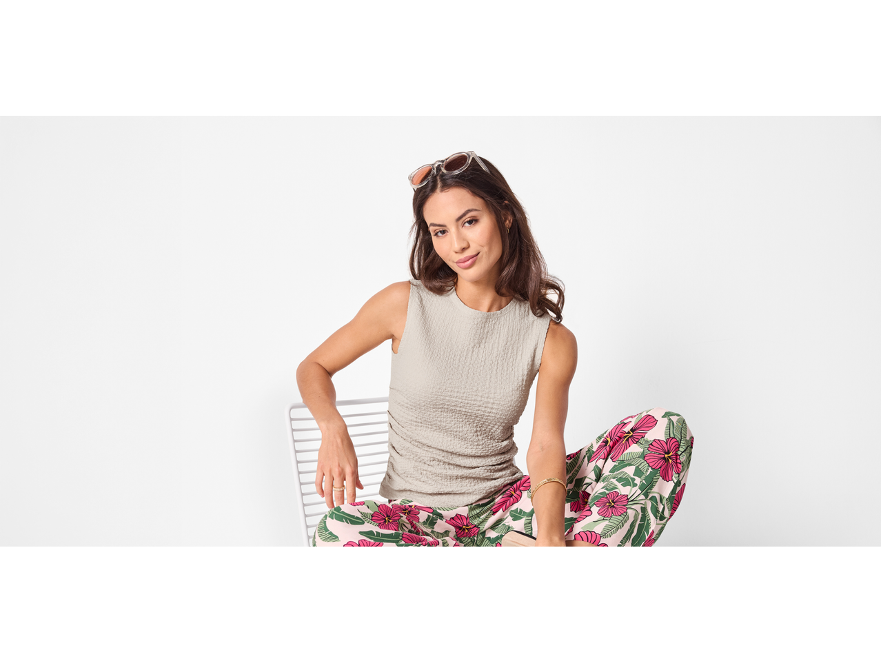 Femeie în top structurat bej ESMARA și pantaloni cu model, așezată pe un scaun alb.