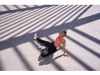 Woman in CRIVIT sports leggings and top, sitting on the ground with striped shadows.