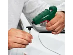 Close-up of a person using a Parkside® hot glue gun to apply glue to a dent repair tool.