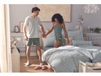 Quarto elegante com um casal de pijama, conjunto de roupa de cama azul claro e vasos decorativos.