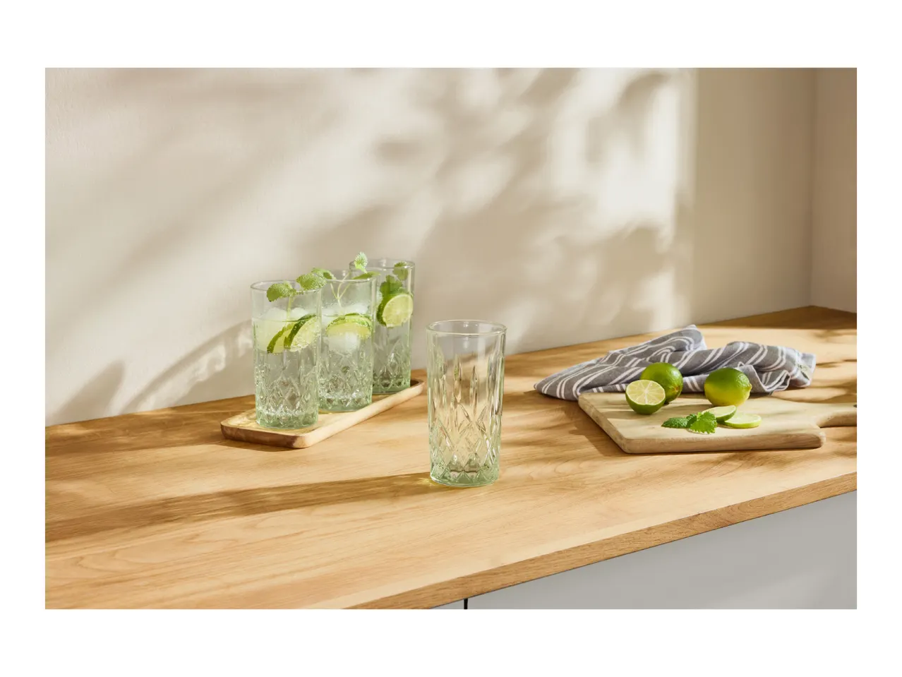 Three glasses of mojito with limes and mint on a wooden countertop.