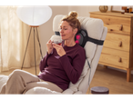 Žena se opušta u fotelji sa SENSIPLAST® Shiatsu masažnim jastukom i šoljom čaja.