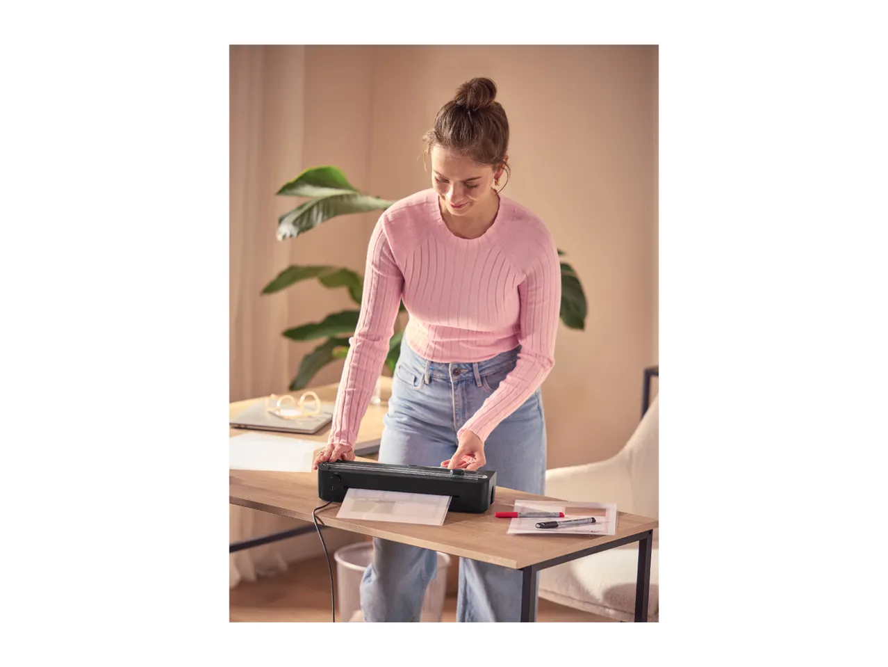 Woman laminating documents with a laminator on a wooden desk.