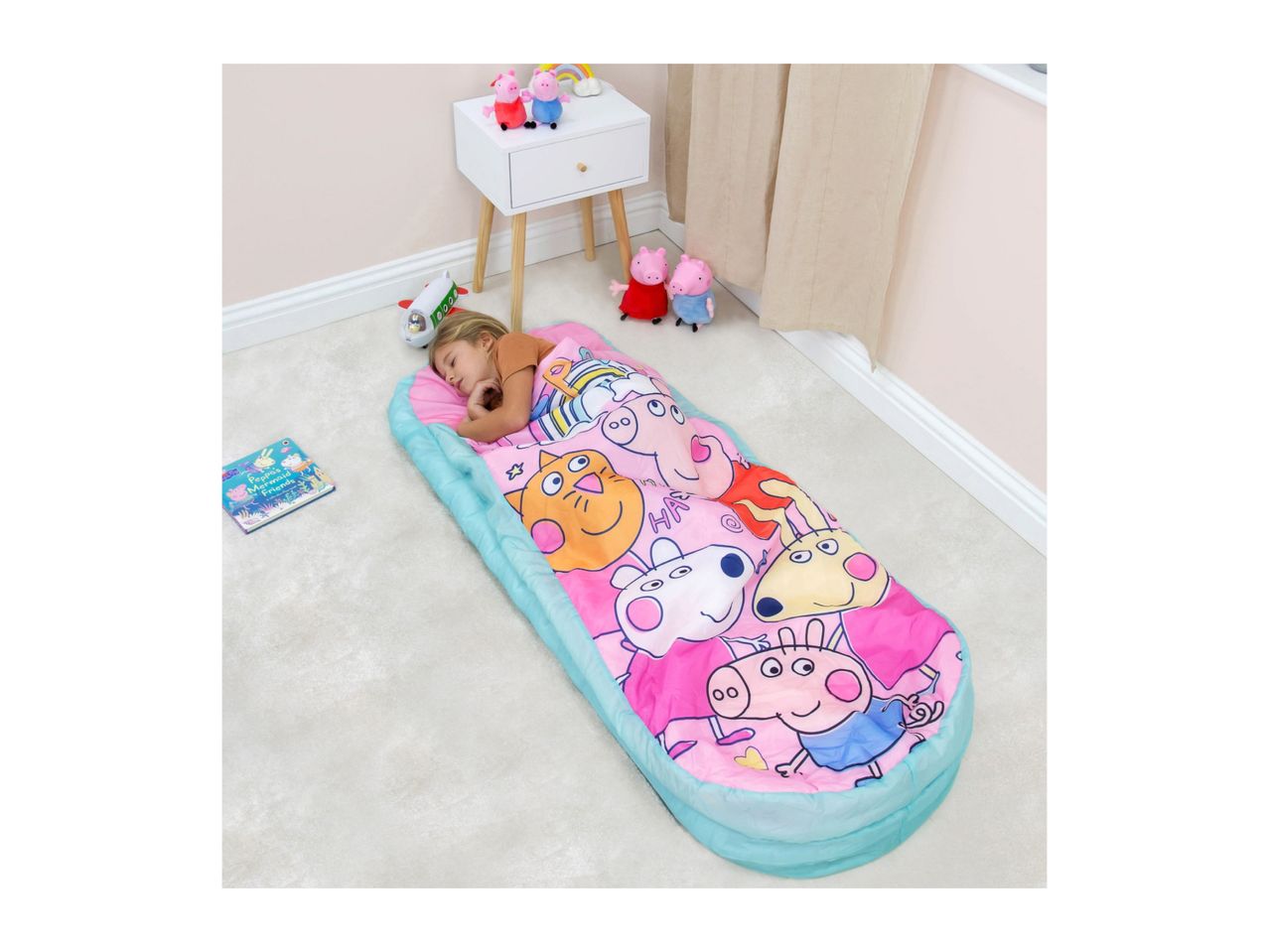 Child sleeping in a pink and blue character sleeping bag on a light carpet.