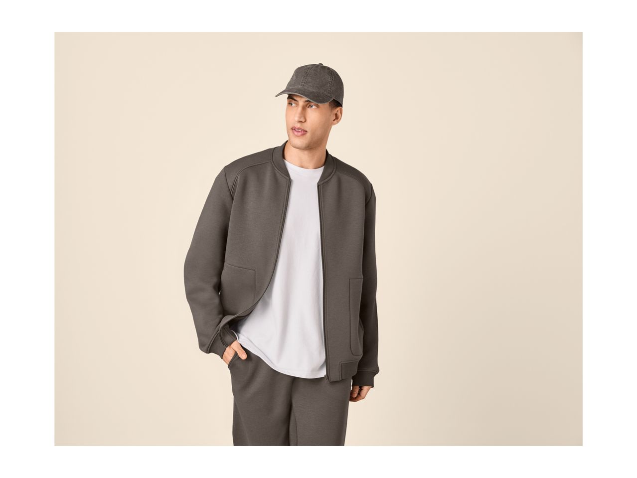 Man in a dark grey bomber jacket, white t-shirt, and matching dark grey sweatpants.