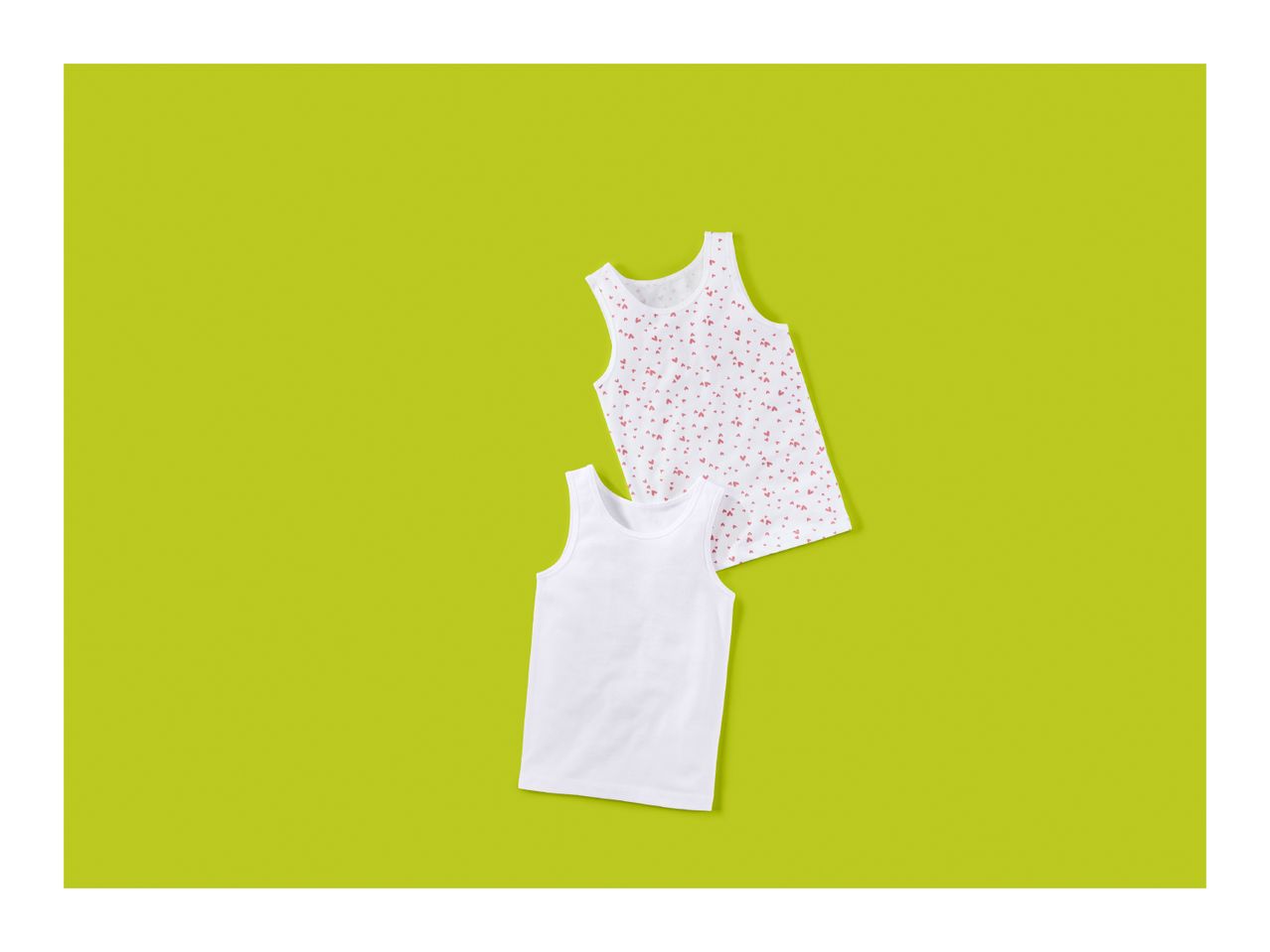 Two children's tank tops, one white and one with a heart pattern, on a green background.