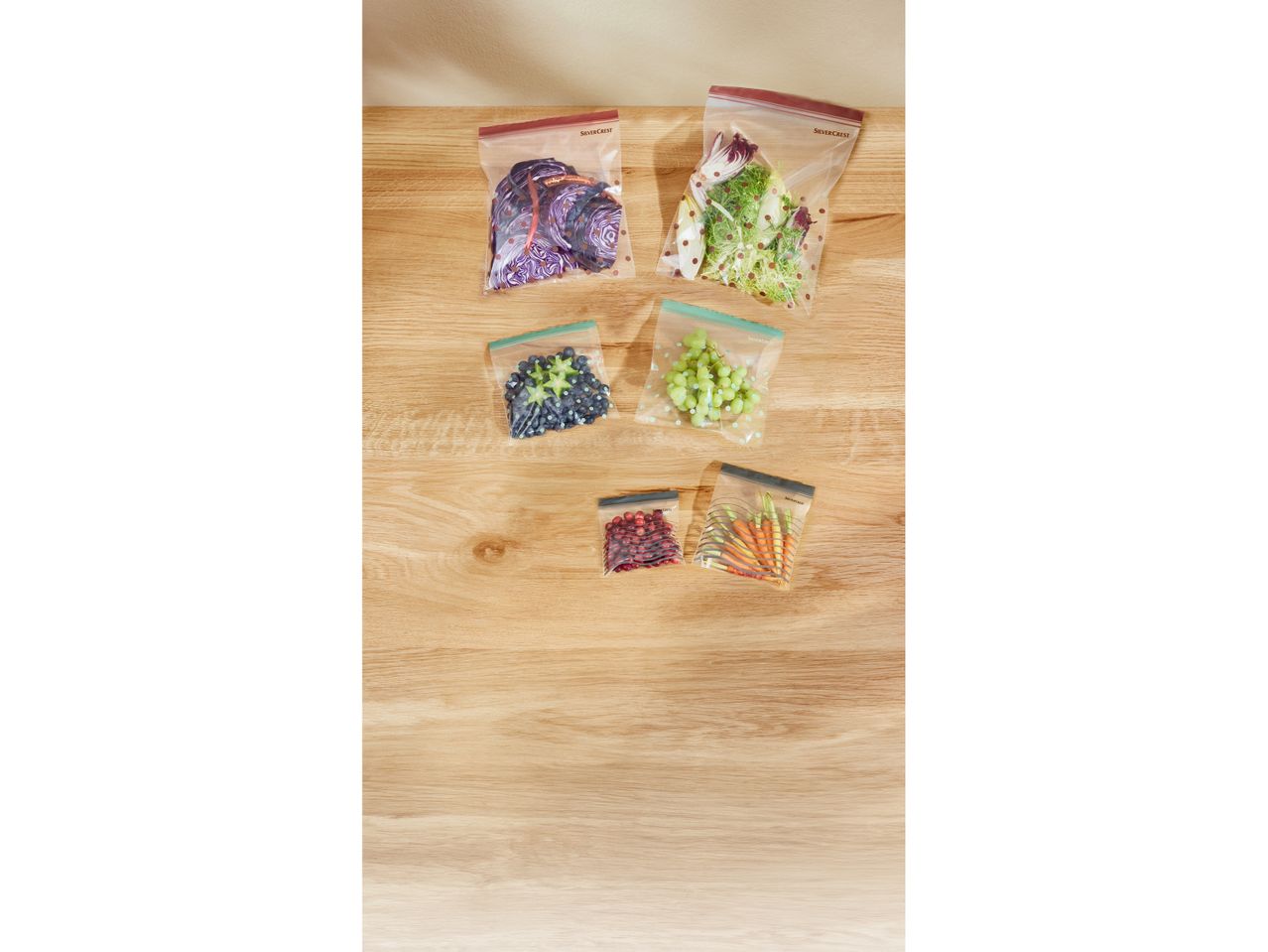 SilverCrest brand reusable food storage bags filled with various fruits and vegetables on a wooden surface.