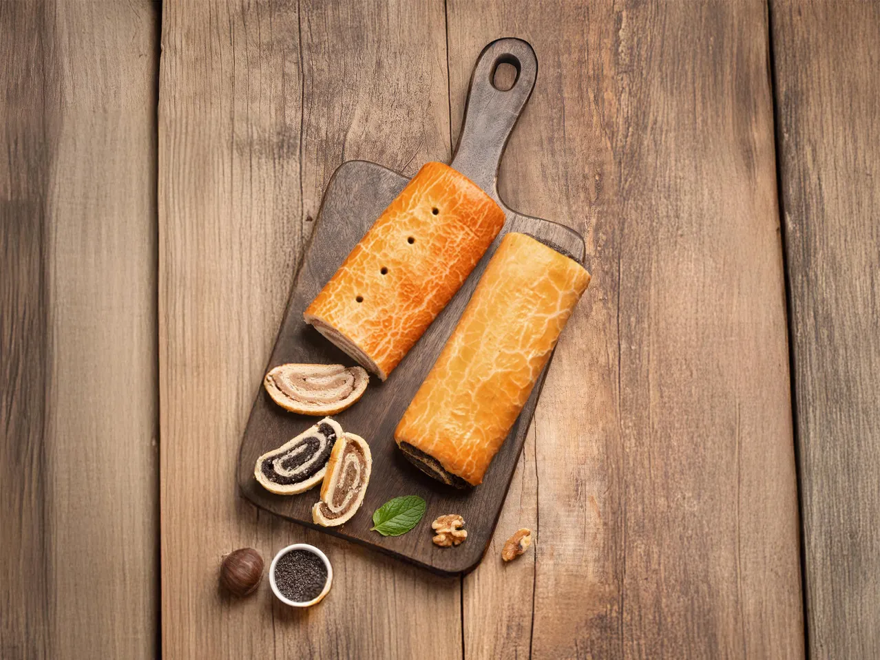 Mákos és diós bejgli szeletekkel, mentával és dióval egy fa vágódeszkán.