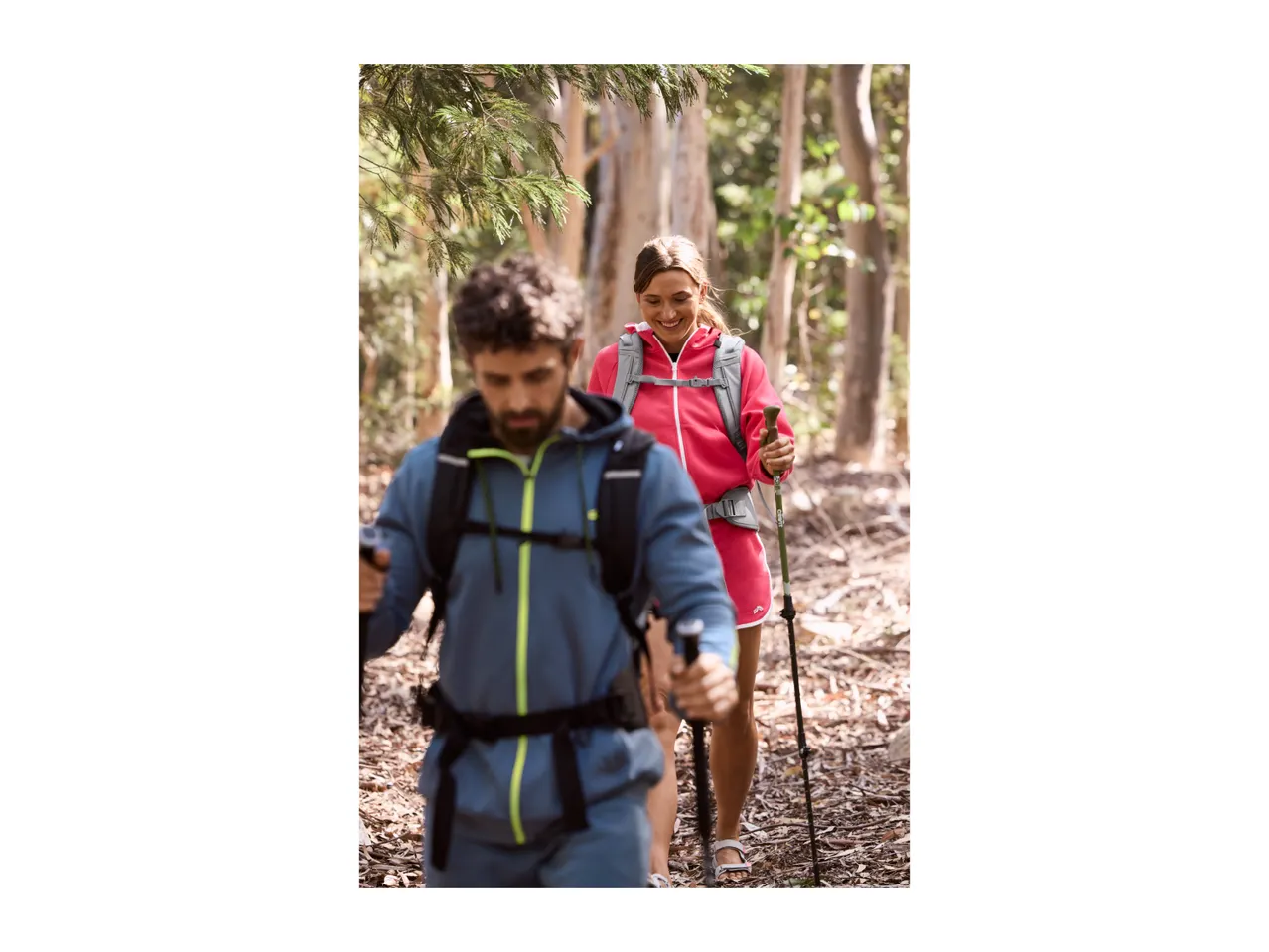 Two hikers with backpacks and walking poles on a forest trail.
