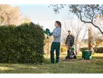 A woman uses a Parkside hedge trimmer while a man uses a leaf blower in a garden.