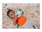 Baby in orange top and grey pants lying on a patterned rug, holding a lion teether.