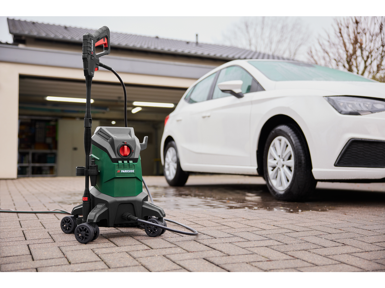 Parkside® 2000W Flexible Pressure Washer next to a white car on a paved driveway.