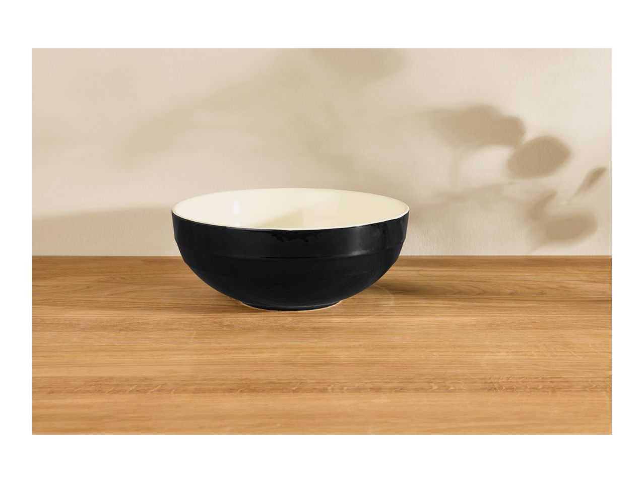 Black and white bowl on a wooden table with plant shadows on the wall.