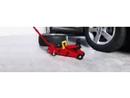 Red car jack and spare tire next to a car, ready for a tire change.
