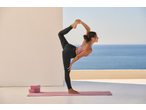 Woman in a pink sports bra and black leggings doing yoga on a mat outdoors.