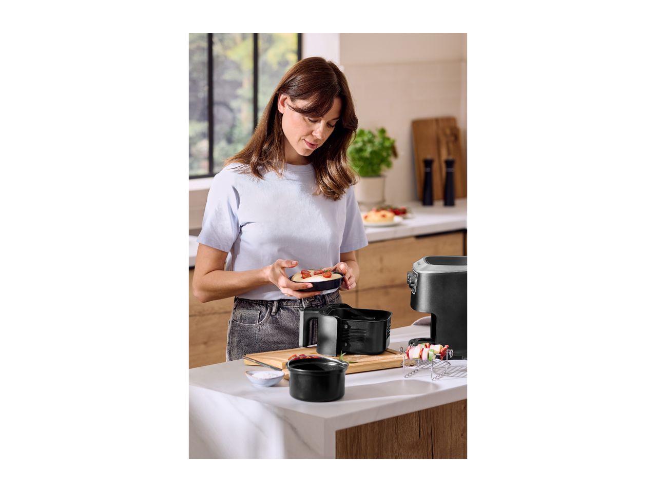 Woman preparing food with an air fryer and accessories in a modern kitchen.