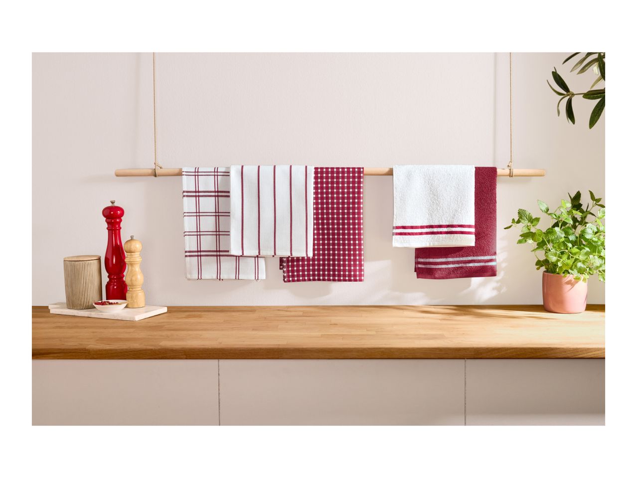 Kitchen towels in red and white patterns hanging on a wooden rod above a countertop.