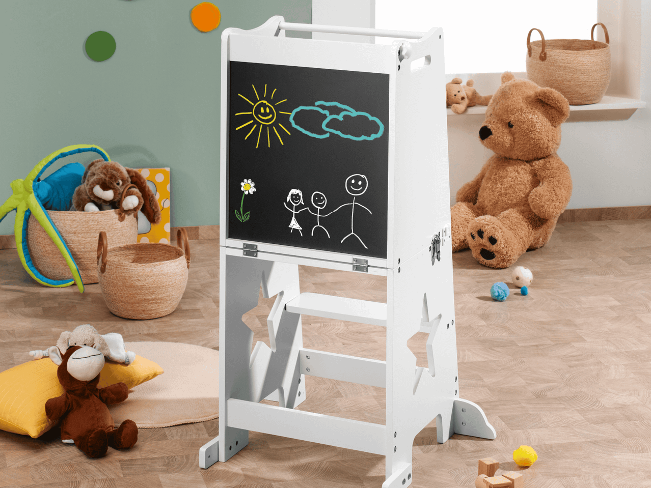 Ein weißes Kinder-Maltisch mit Kreidezeichnungen in einem Spielzimmer mit Spielzeug.